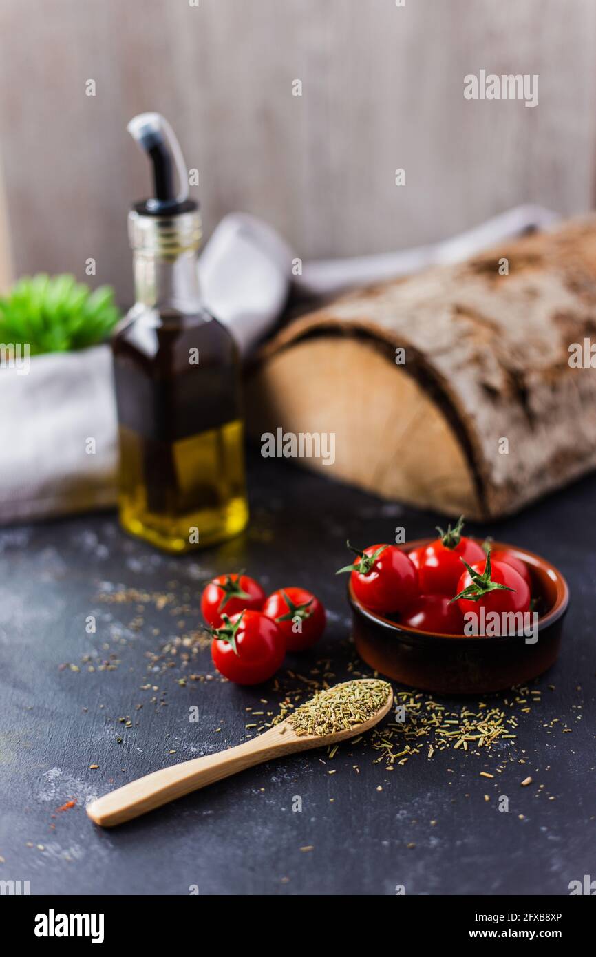 Spoon with spices, cherry tomatoes and a bottle of olive oil on a dark table Stock Photo