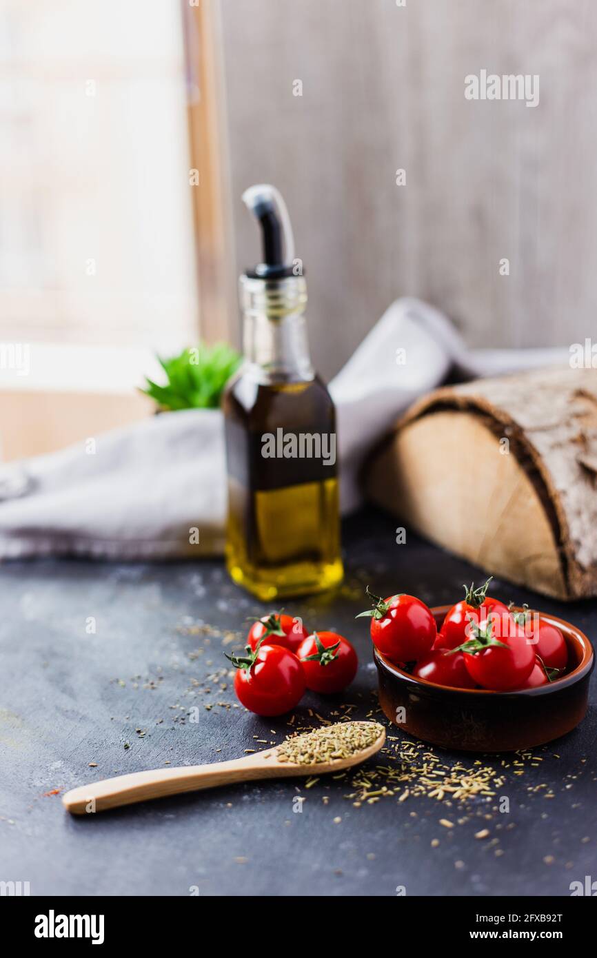 Spoon with spices, cherry tomatoes and a bottle of olive oil on a dark table Stock Photo