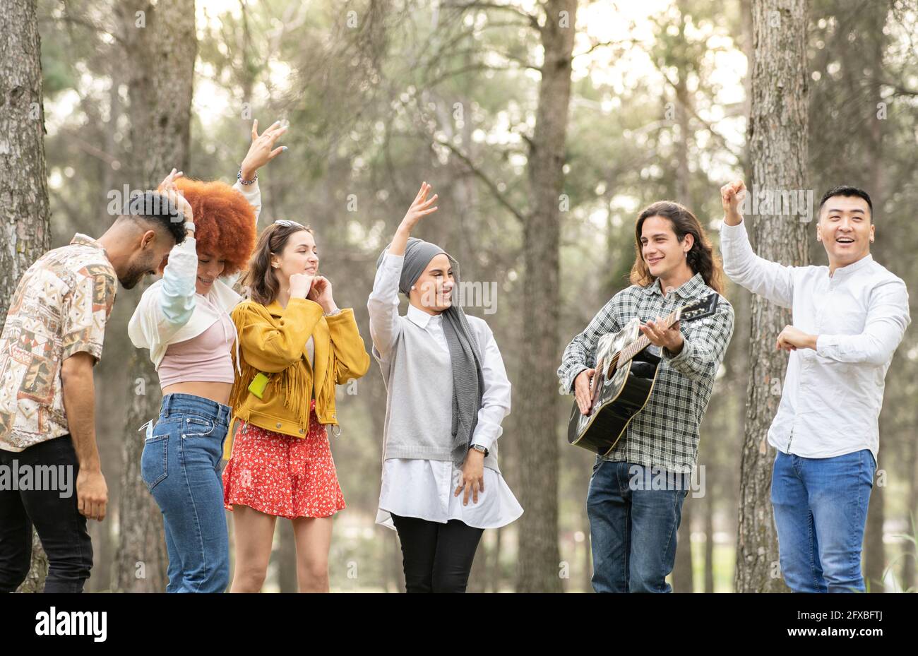 Cheerful multi-ethnic female and male friends dancing and enjoying in forest Stock Photo