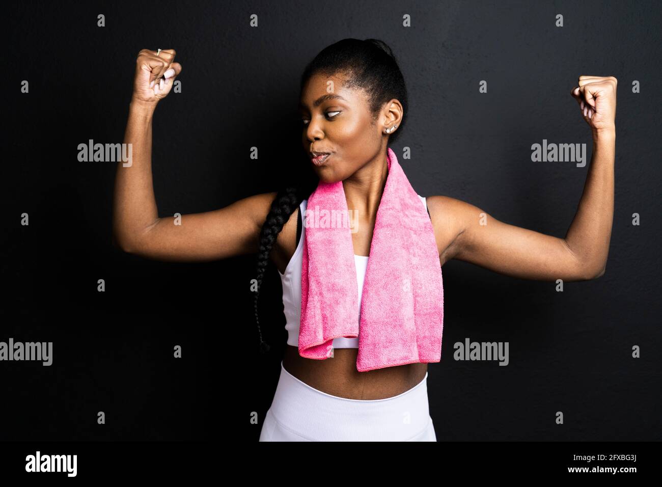Active woman flexing biceps while standing against black background Stock Photo