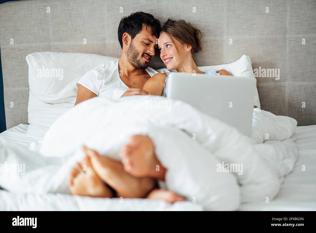 Smiling couple looking at each other while sitting on bed Stock Photo