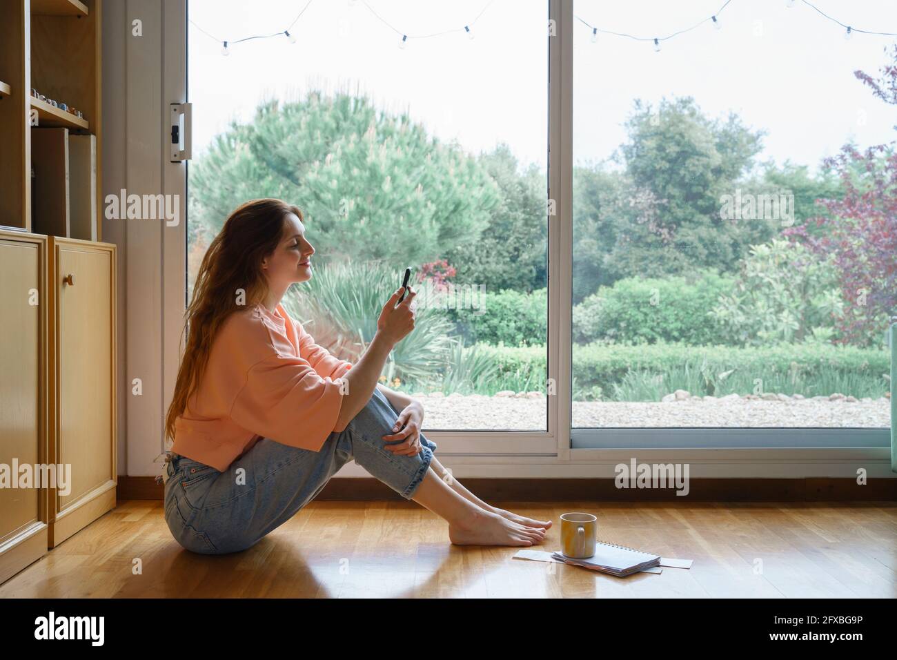 Smiling woman using smart phone while sitting at home Stock Photo