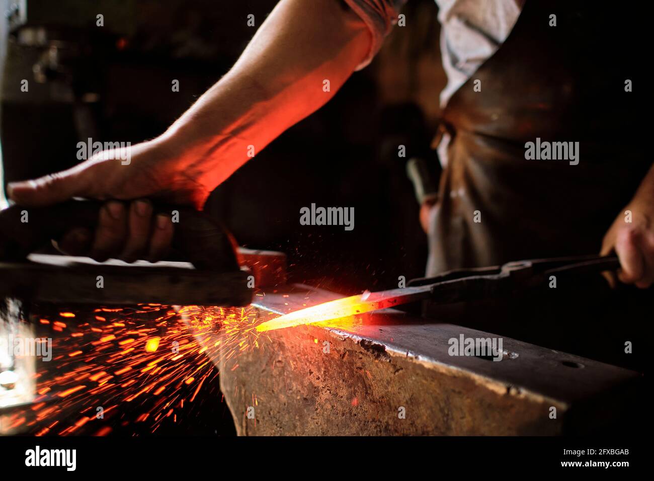Male expert forging overheated metal on anvil at blacksmith shop Stock Photo