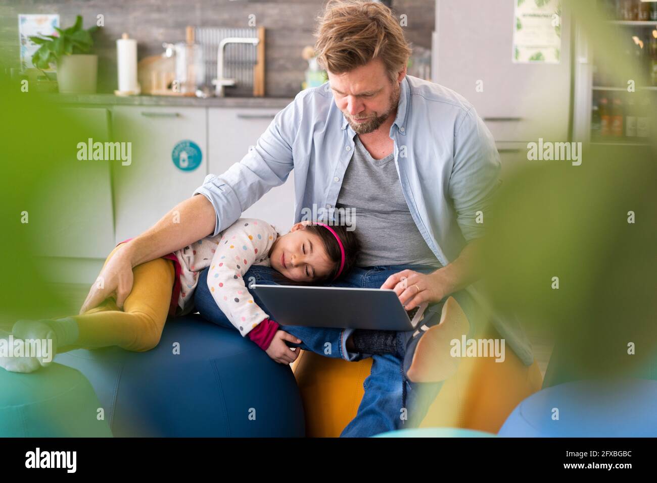 Businessman using laptop while daughter lying on lap at home Stock Photo