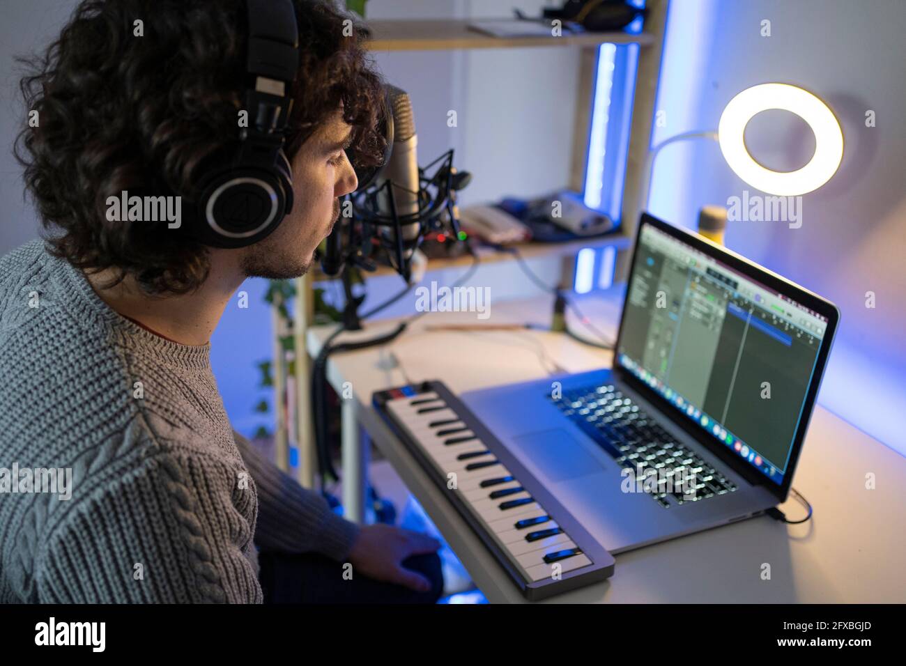 Young music composer with headphones and piano using laptop at home Stock Photo
