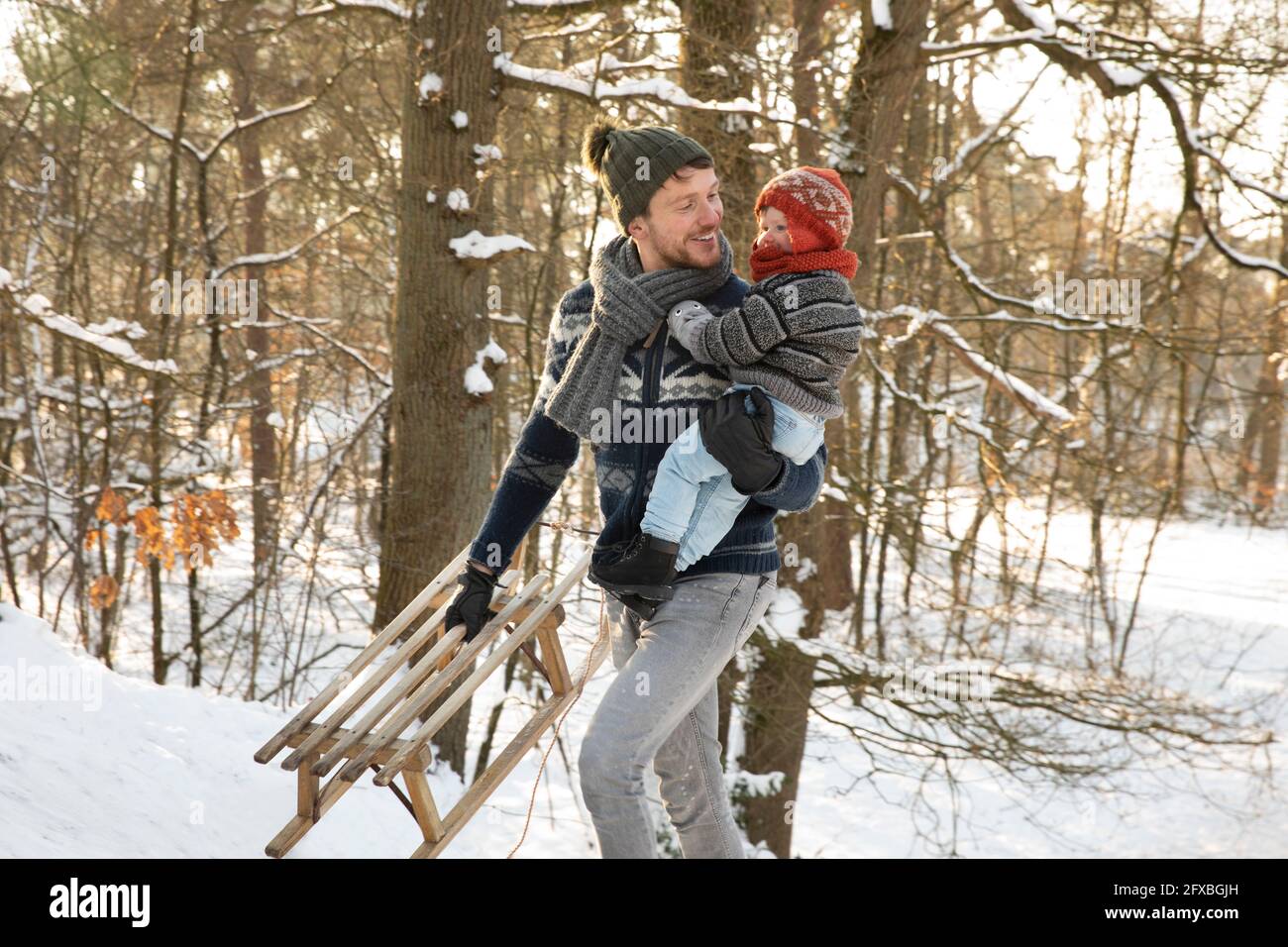 Father with sled holding son while walking in snow during winter Stock Photo
