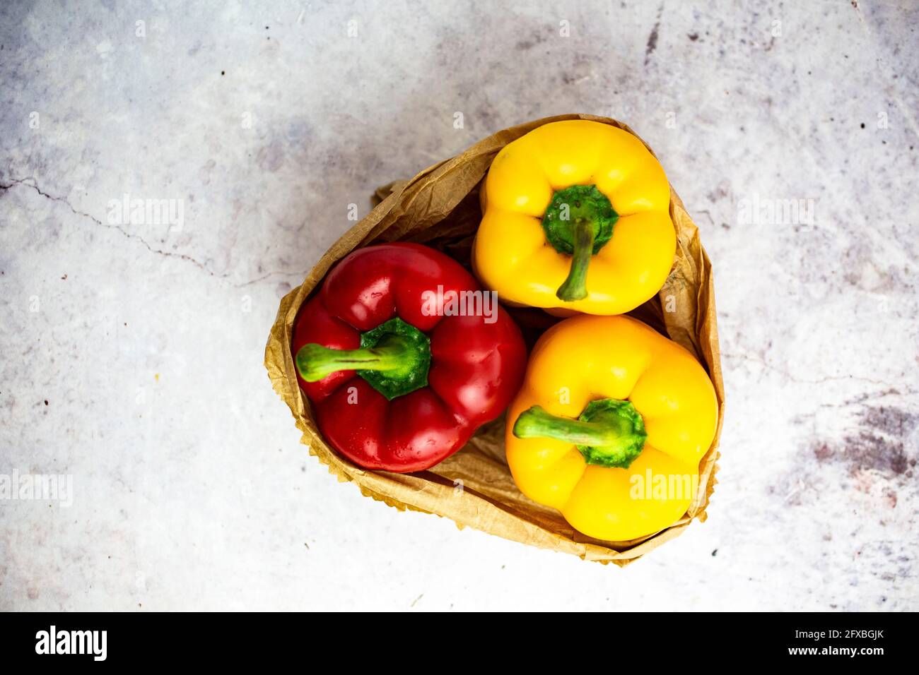 Studio shot of paper bag with single red and two yellow bell peppers Stock Photo