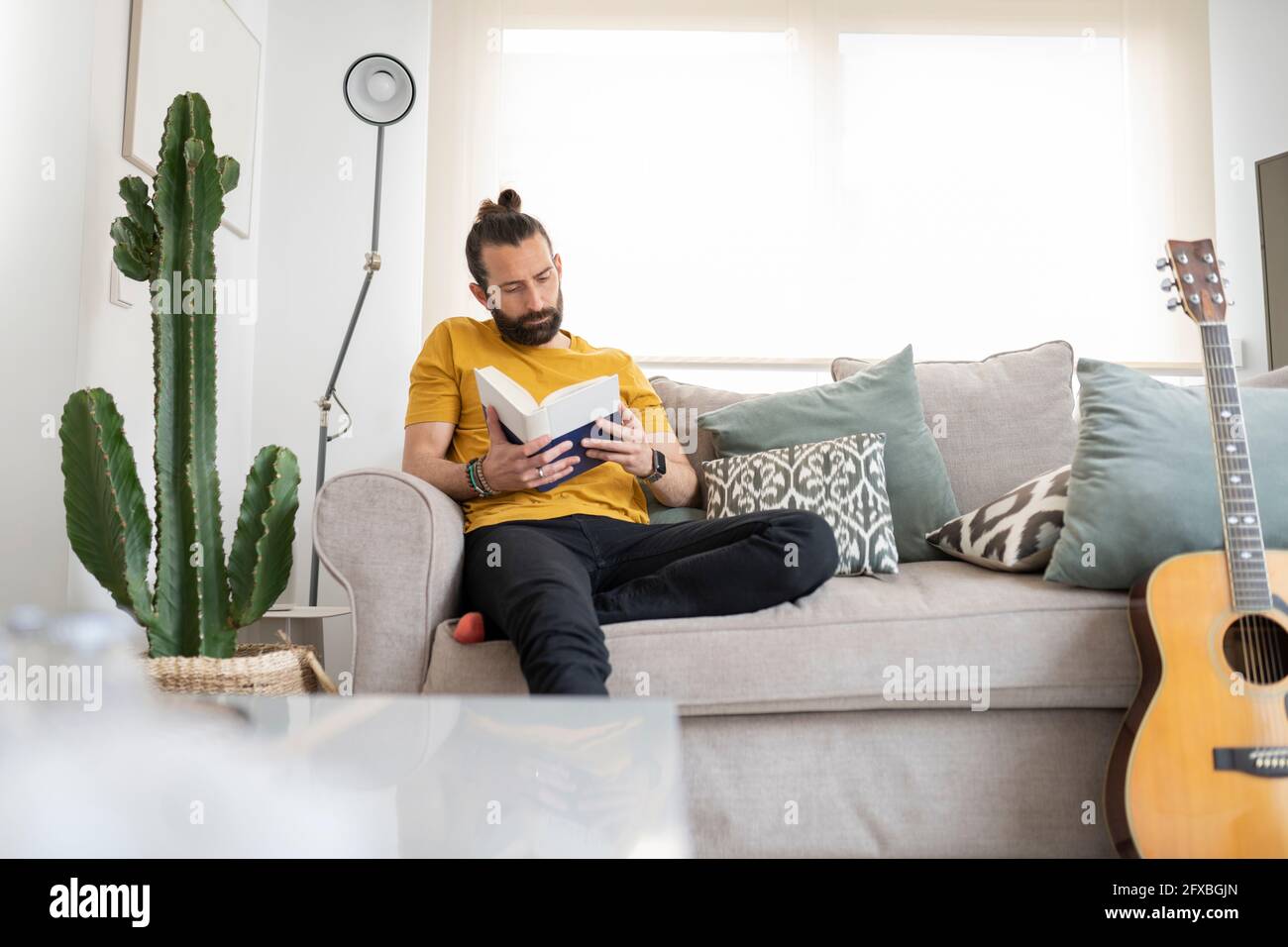 Handsome man reading book while sitting on sofa at home Stock Photo