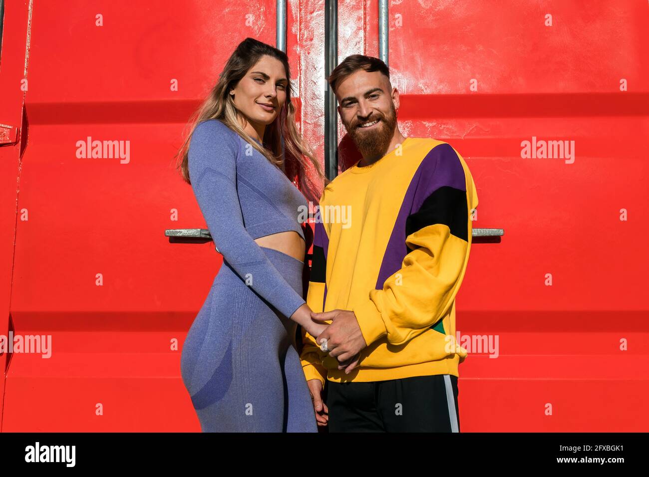 Smiling couple holding hands while standing in front of red container Stock Photo