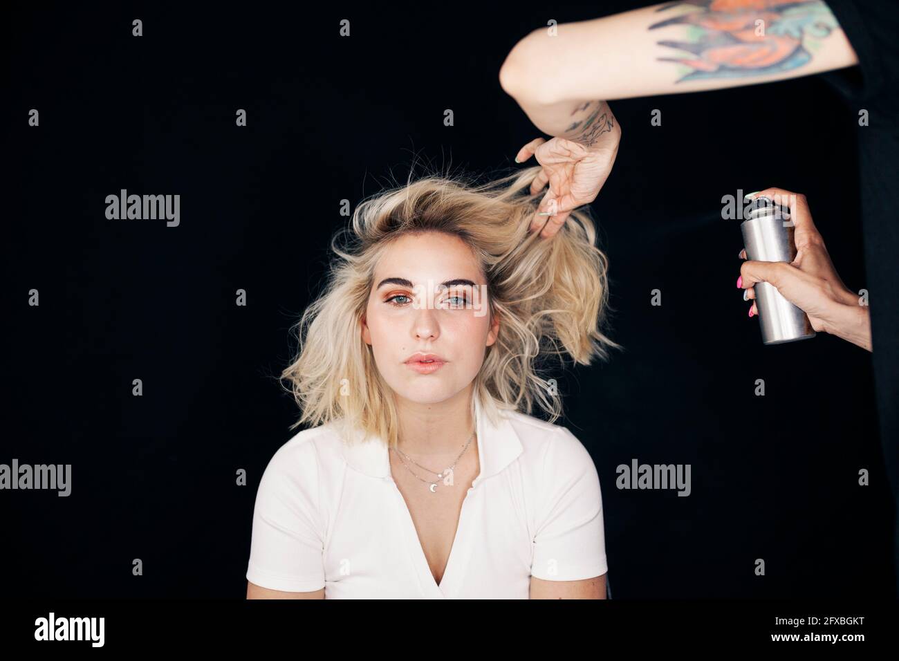 Female stylist applying spray on model's hair in studio Stock Photo