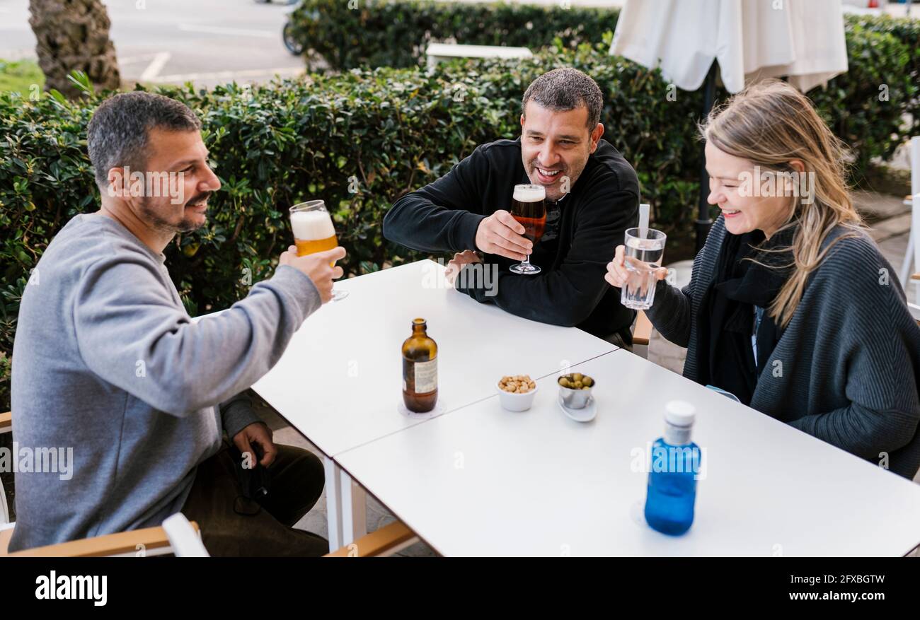 Happy male and female friends enjoying drinks sitting at bar terrace ...