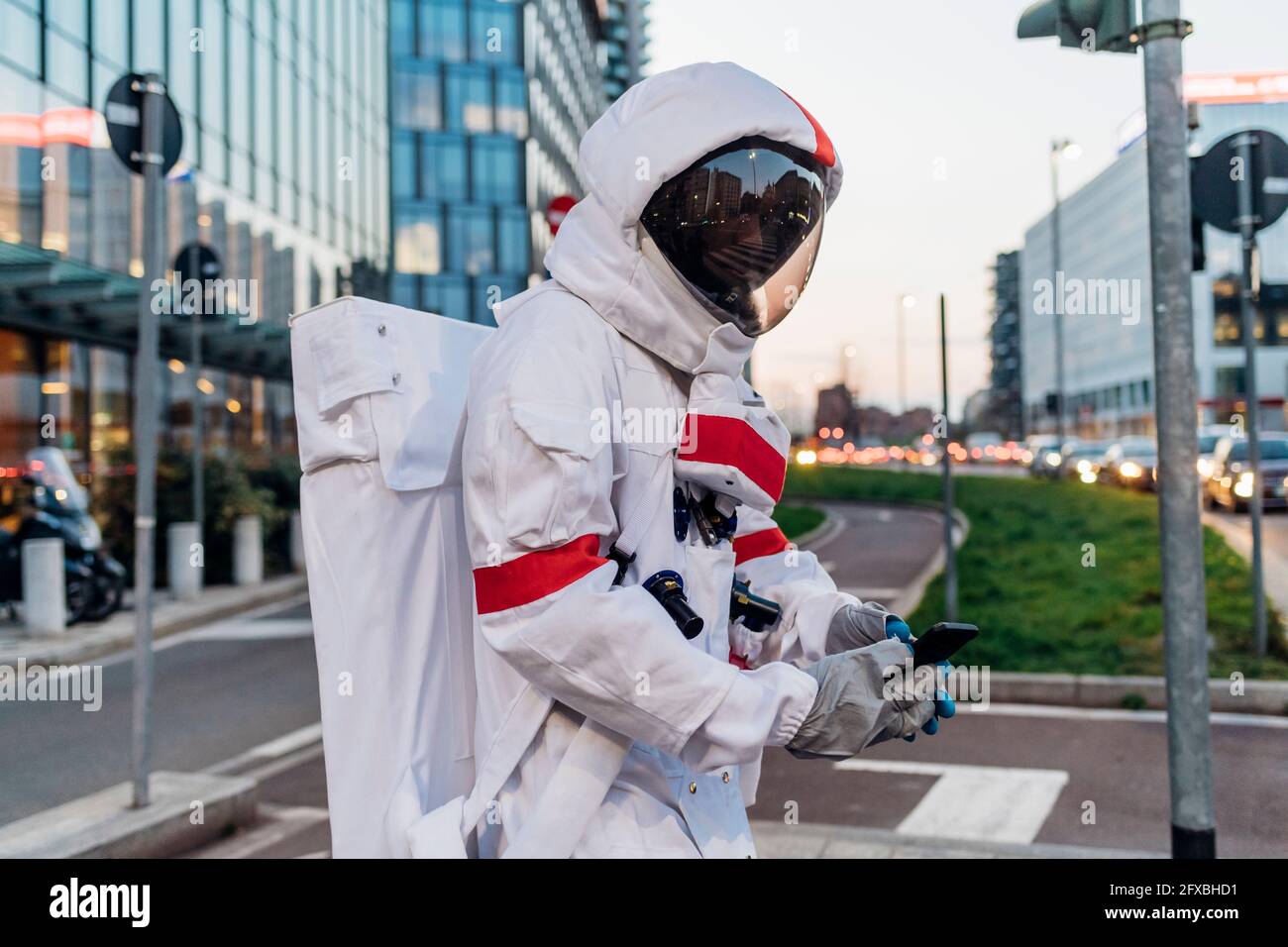 Male astronaut wearing space suit using mobile phone in city street ...