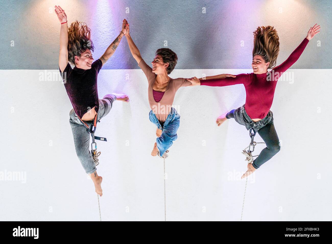 Smiling dancer holding hands while hanging on rope in dance studio