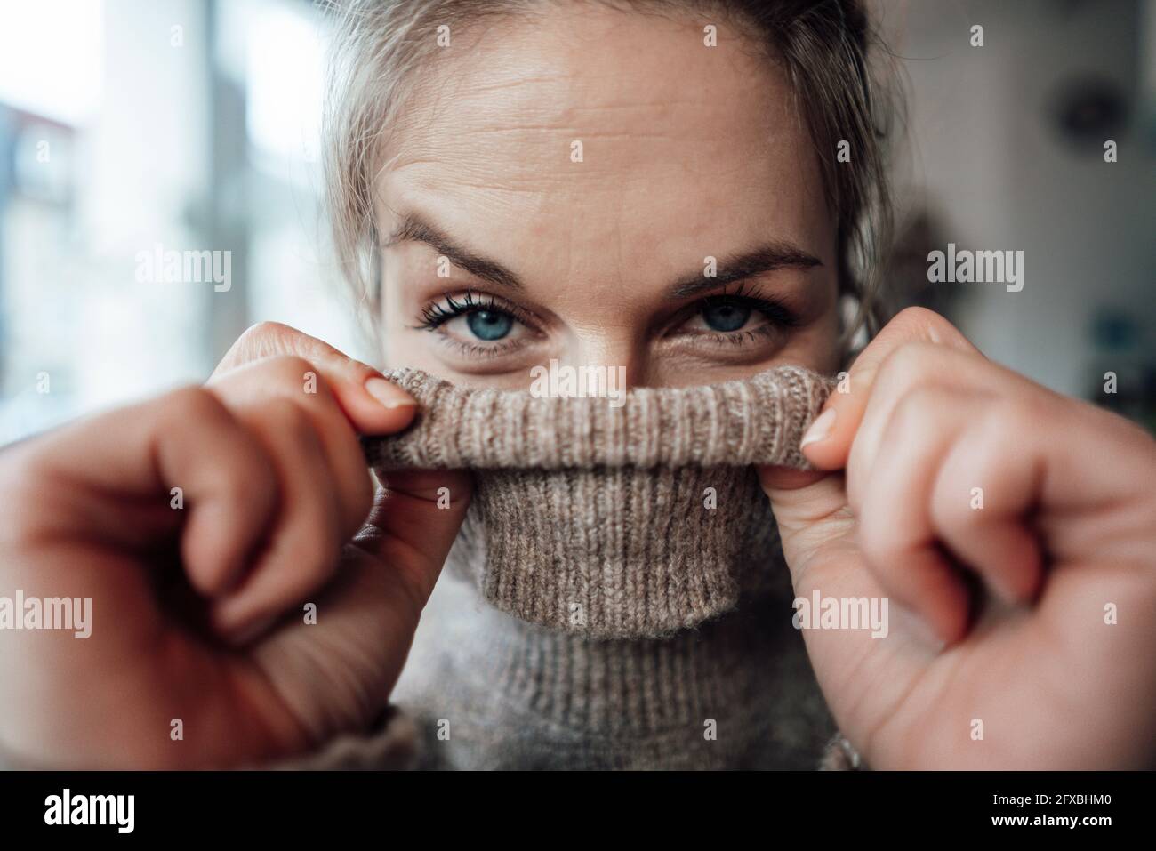 Playful woman covering face in sweater at cafe Stock Photo - Alamy