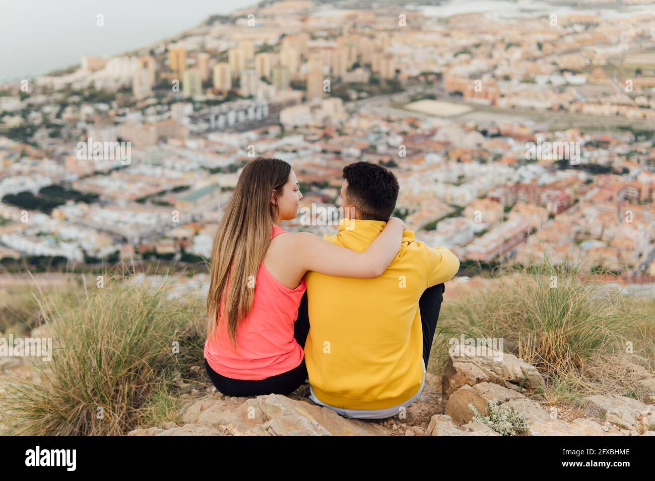 Young girlfriend sitting with arm around of boyfriend on hill Stock Photo