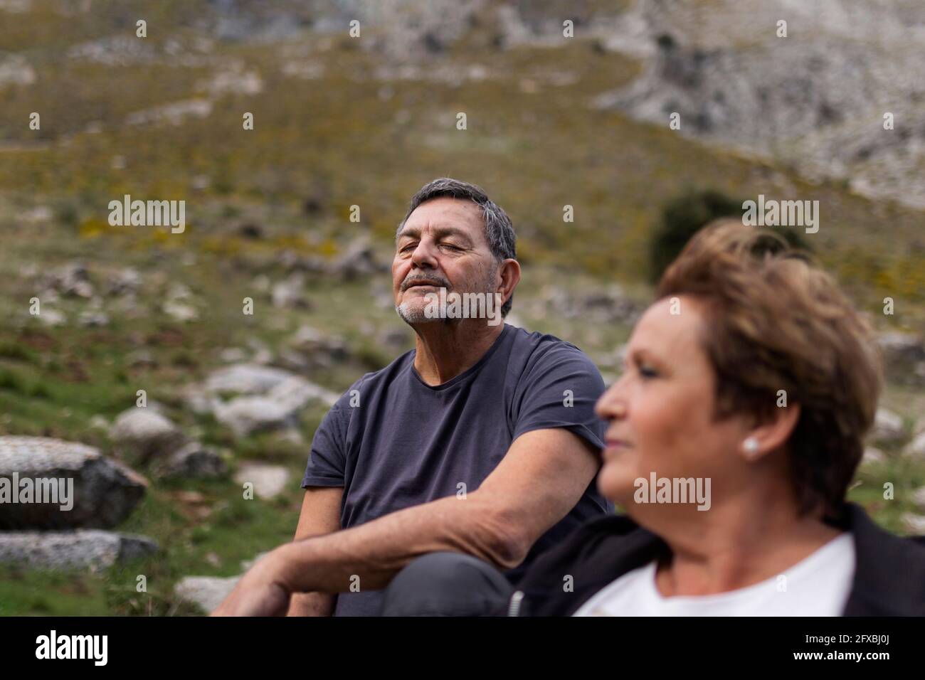 Senior woman with man sitting in background, taking a break in ghe mountains Stock Photo