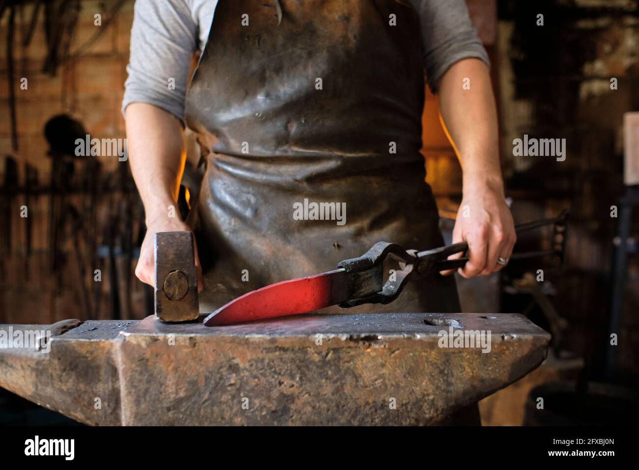 Blacksmith making knife of metal on anvil at blacksmith shop Stock Photo