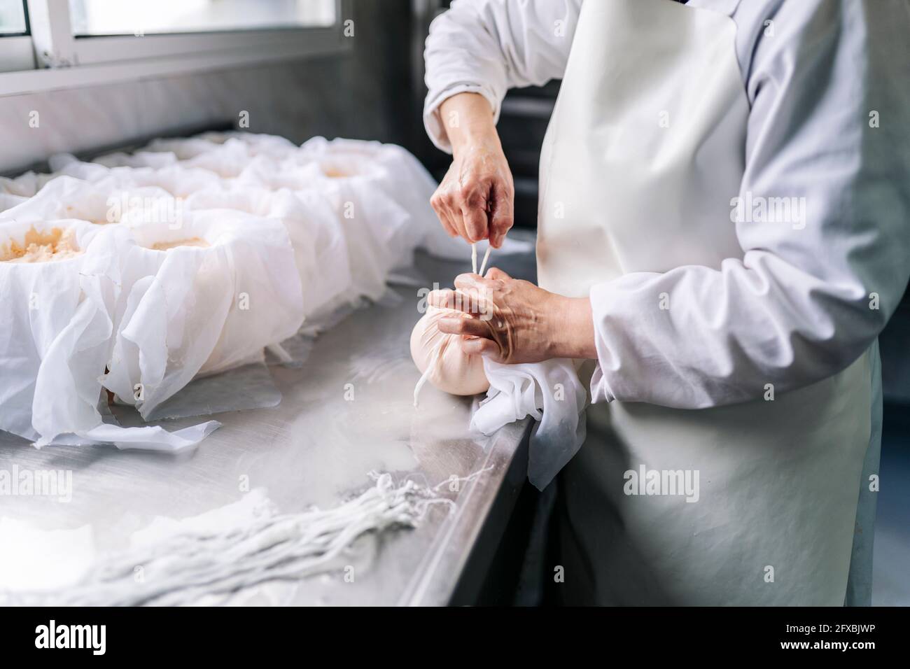 Skilled chef wrapping cheese in cloth at factory Stock Photo