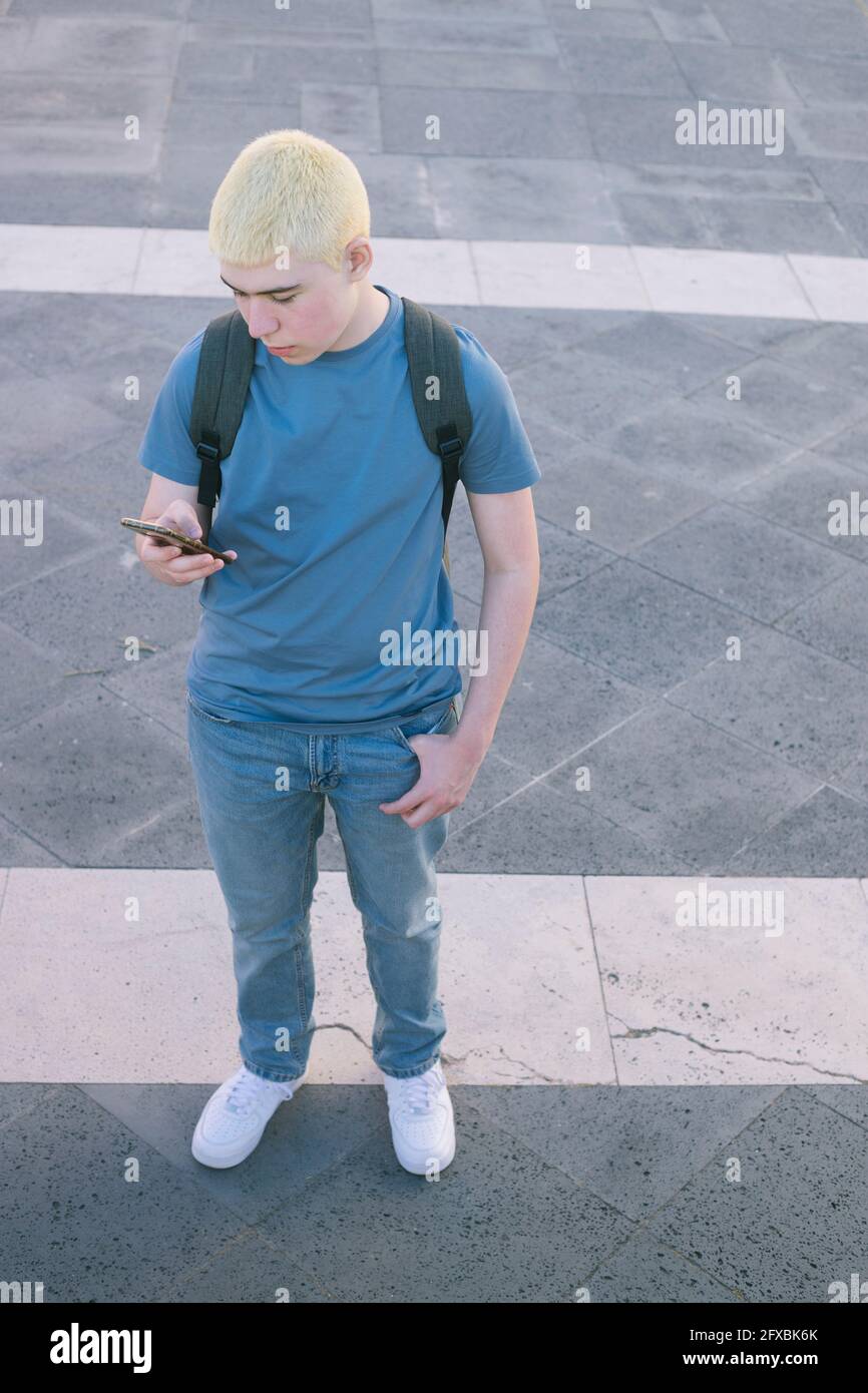 teenager standing with backpack looking at cell phone screen Stock Photo