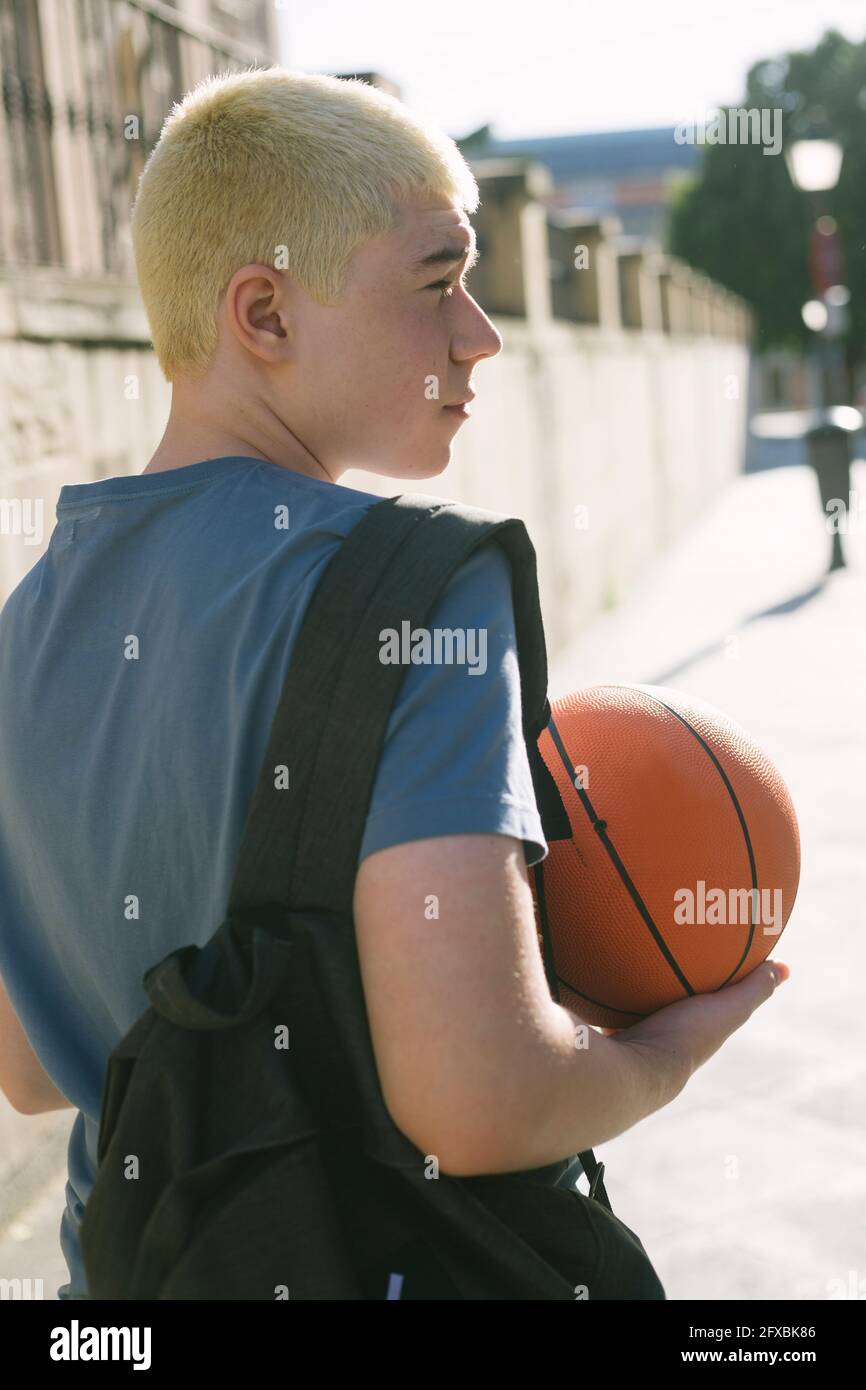 teenager with backpack and basketball walking in the street Stock Photo