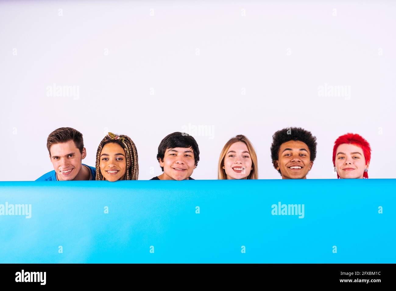 Smiling multi-ethnic male and female friends behind blue backdrop Stock Photo