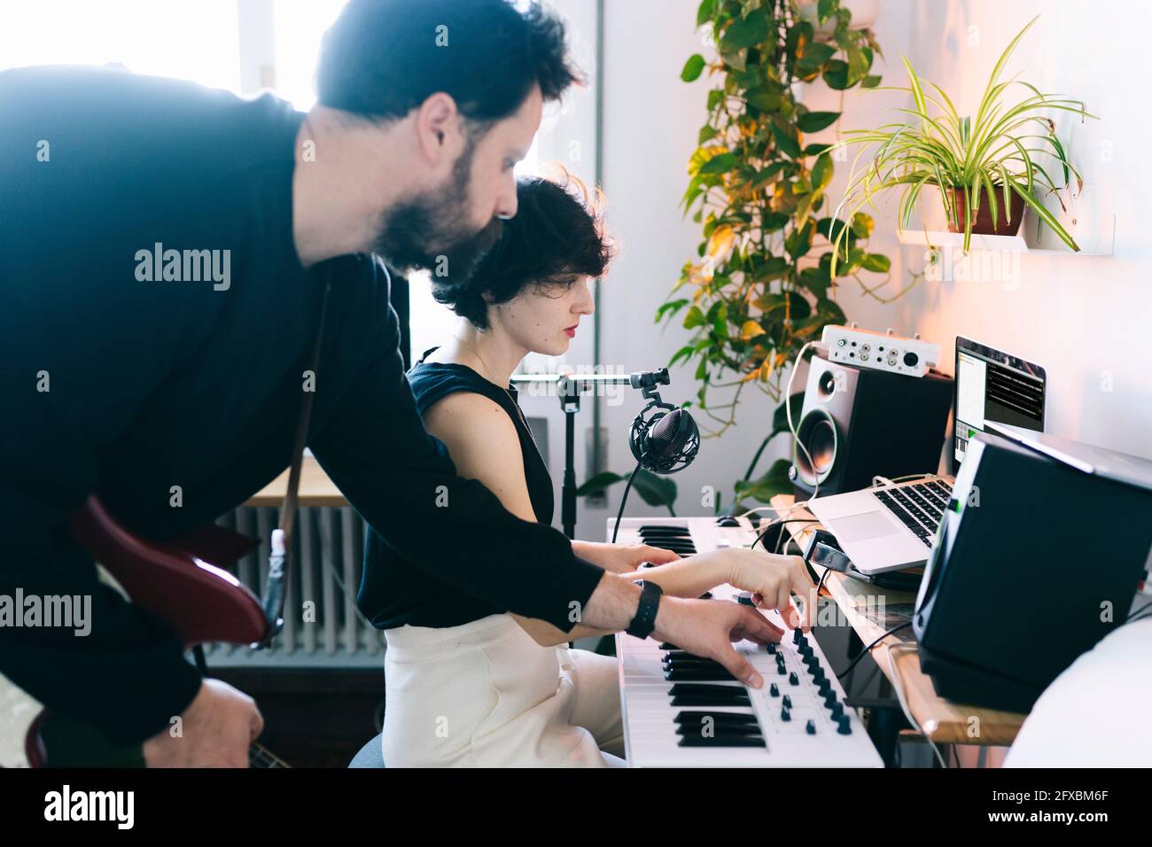 Male musician helping female composer with electric piano in studio Stock Photo