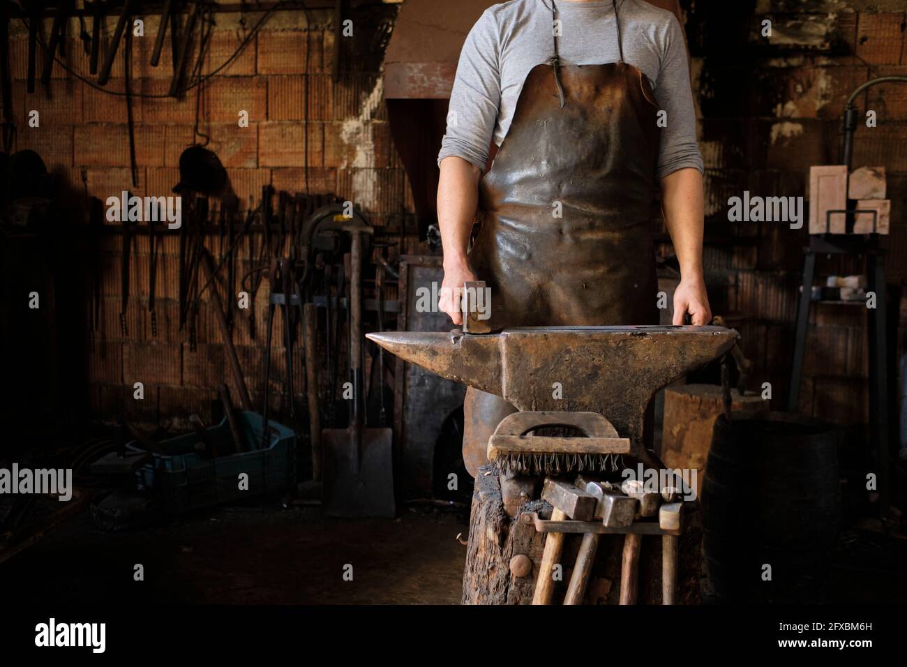 Male blacksmith standing with hammer by anvil at shop Stock Photo