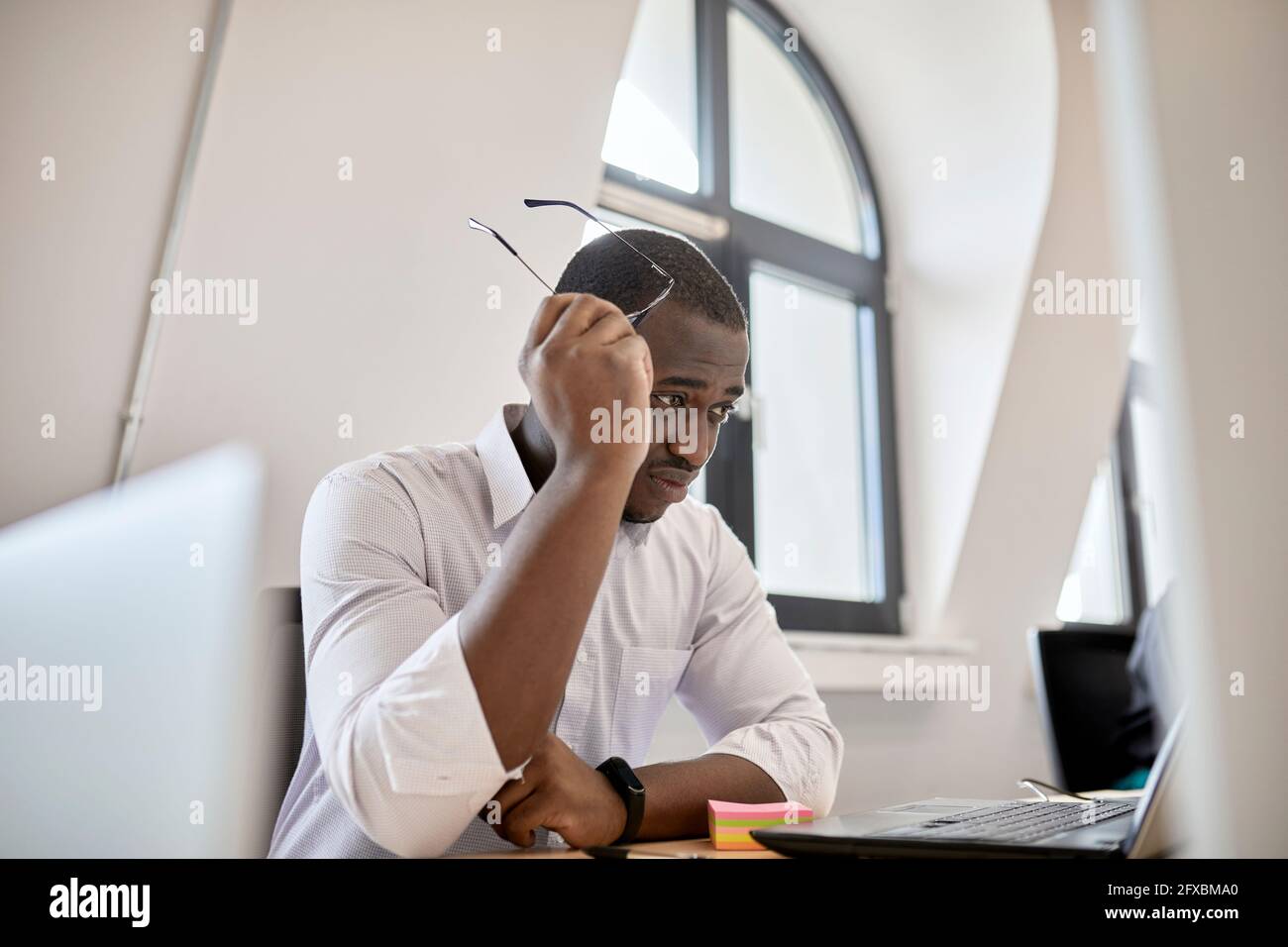 Worried male professional holding eyeglasses while looking at laptop in office Stock Photo