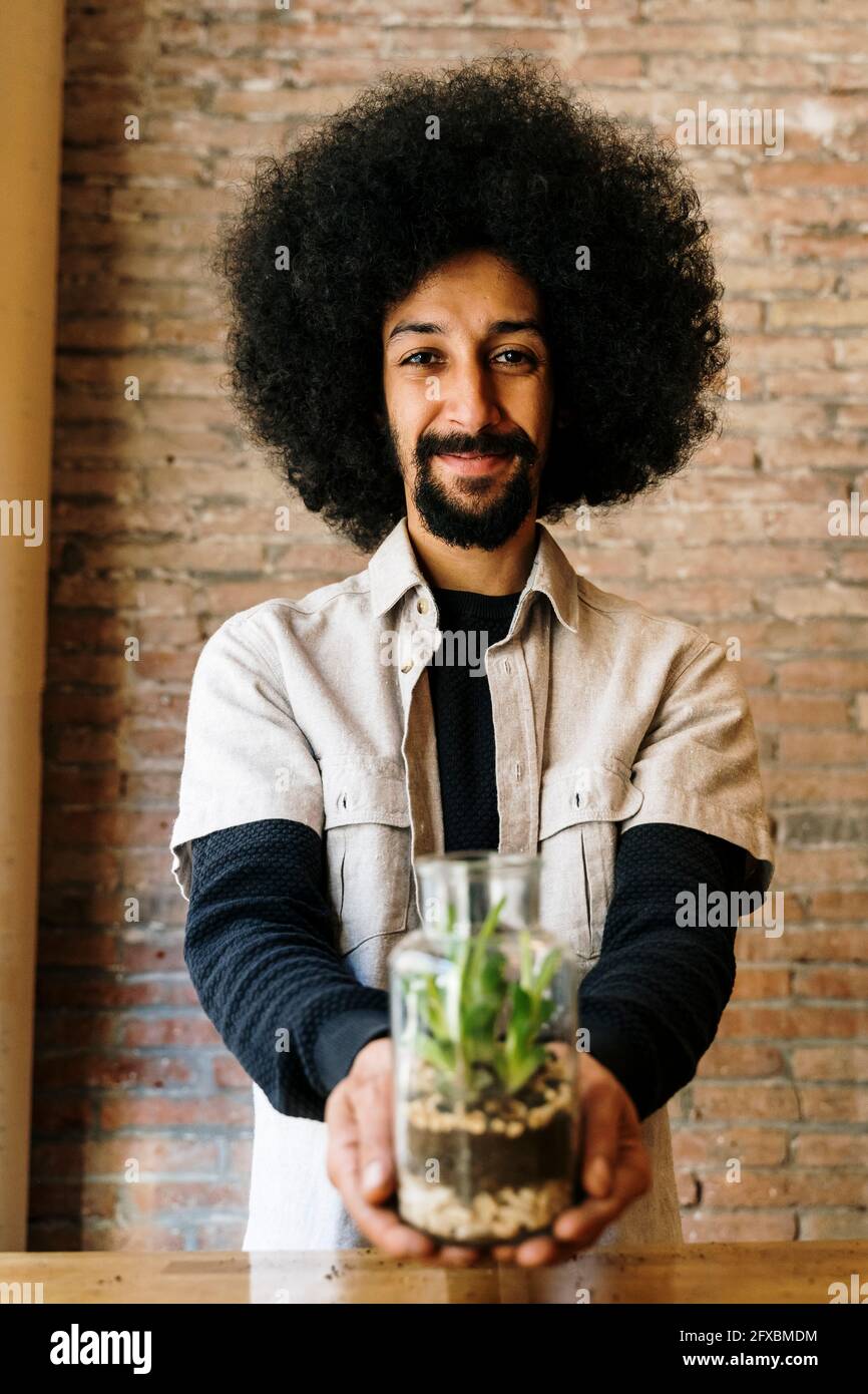 Smiling male gardener holding glass jar with succulent plant Stock Photo