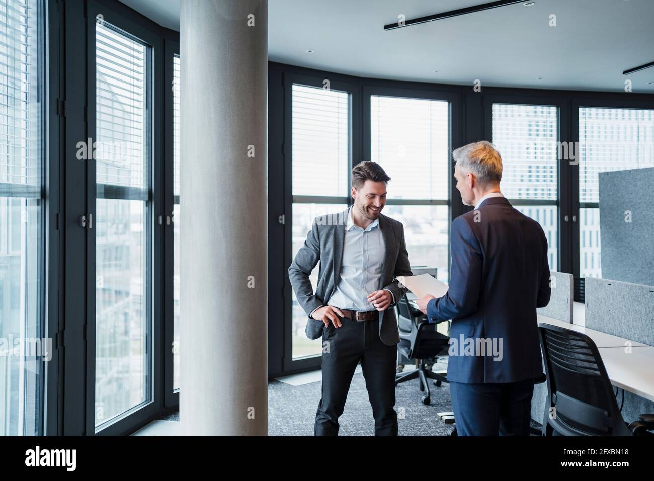 Male professional discussing over documents by architectural column in office Stock Photo