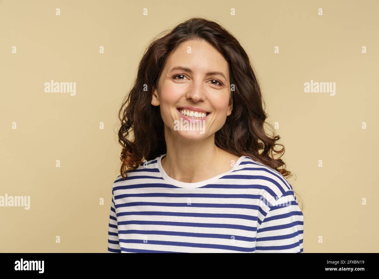 Portrait of curly millennial female, studio shot. Young woman with happy toothy smile and clean skin Stock Photo