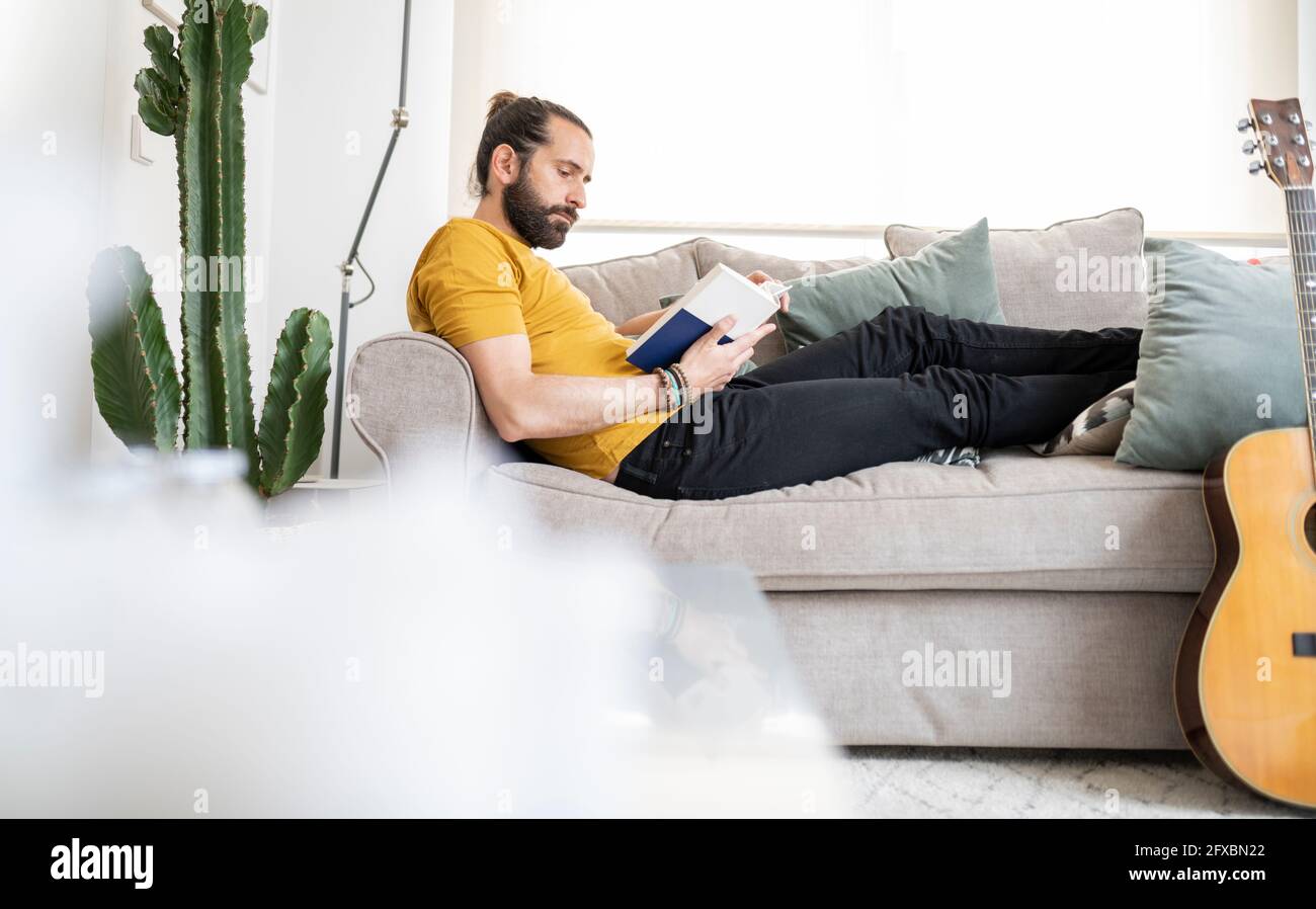 Man reading book while relaxing on sofa at home Stock Photo