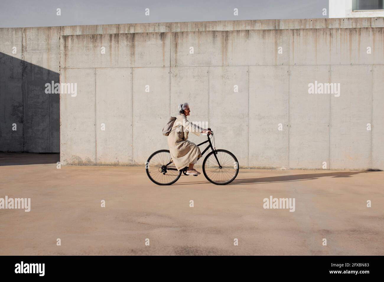 Woman cycling by wall on footpath Stock Photo