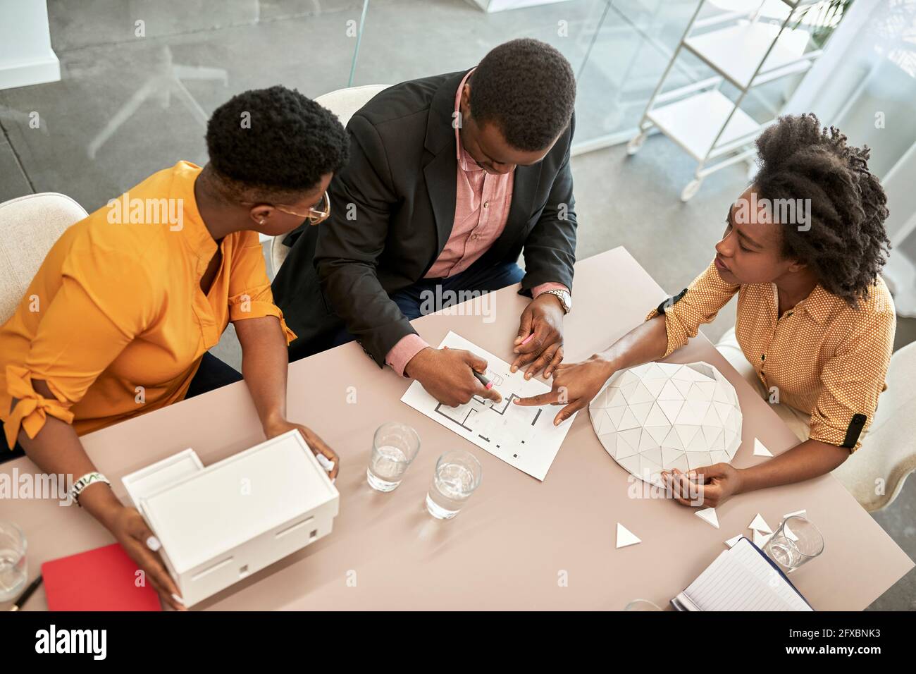 Female architect discussing over blueprint with colleagues in office Stock Photo