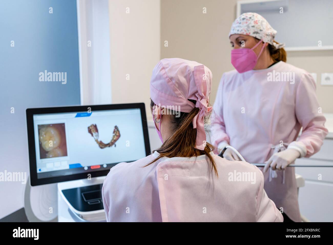 Female dentists wearing surgical cap examining digital image of teeth on screen at clinic Stock Photo
