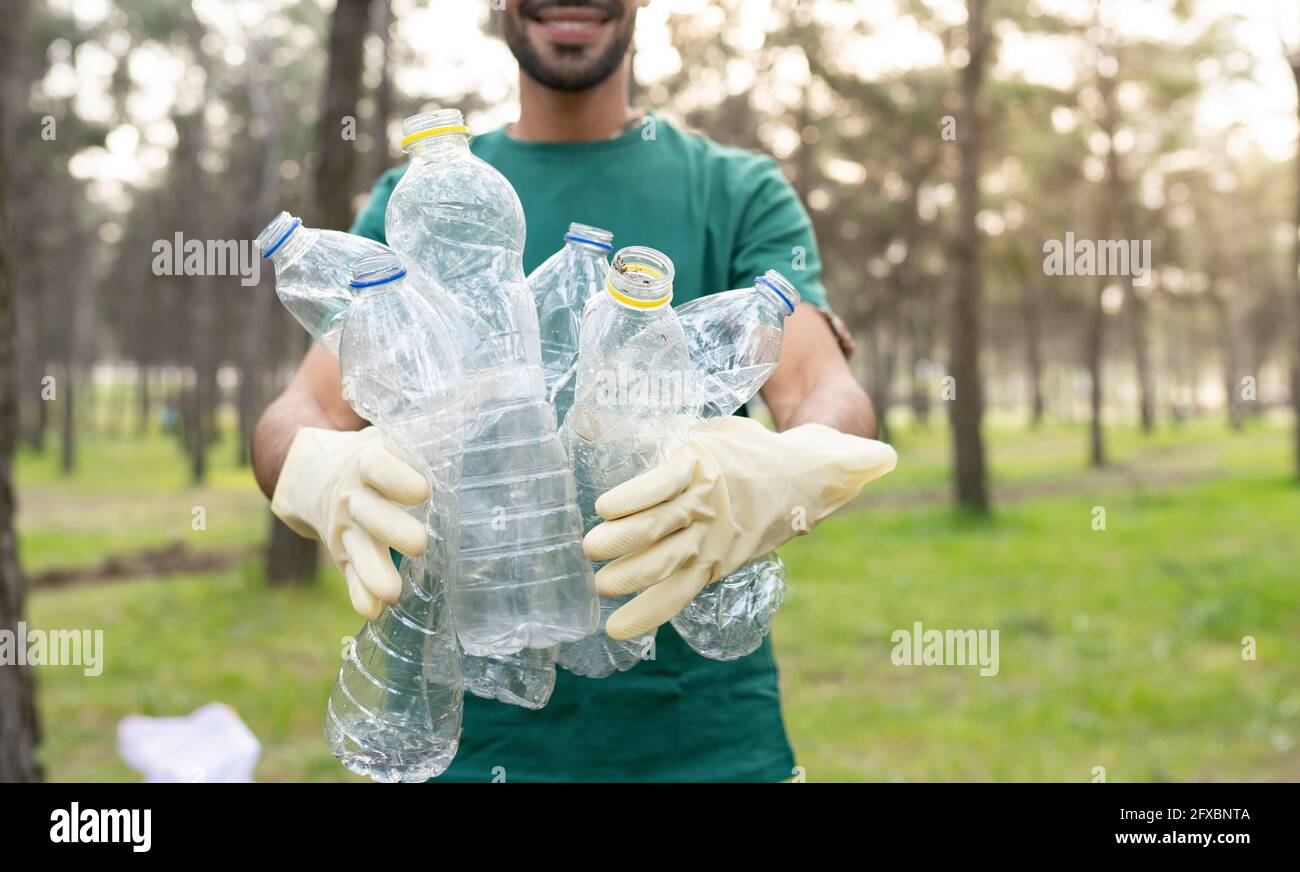 Male volunteer holding plastic bottles while cleaning forest Stock Photo