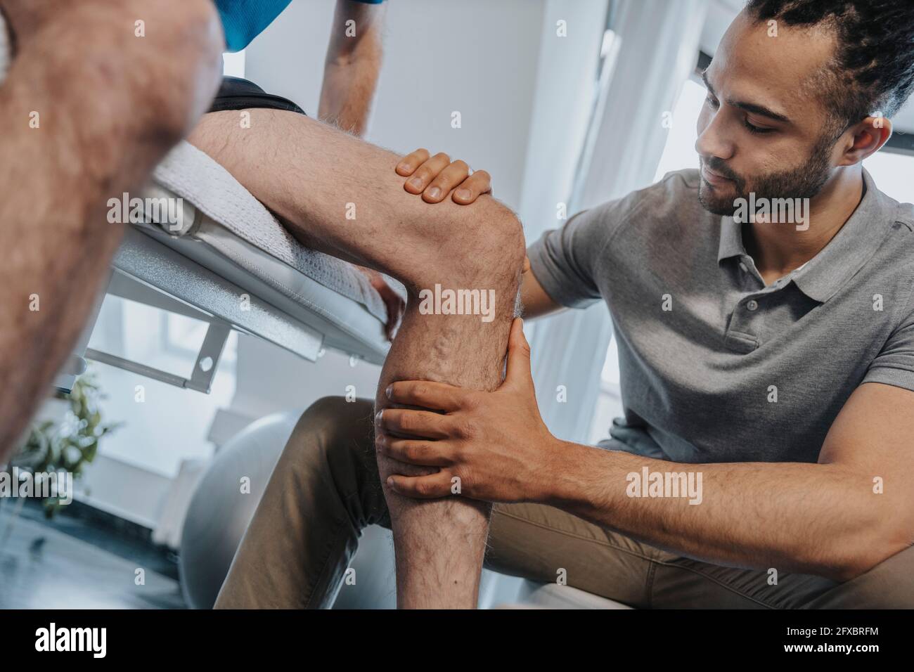 Male Physical therapist examining knee of patient in practice Stock Photo