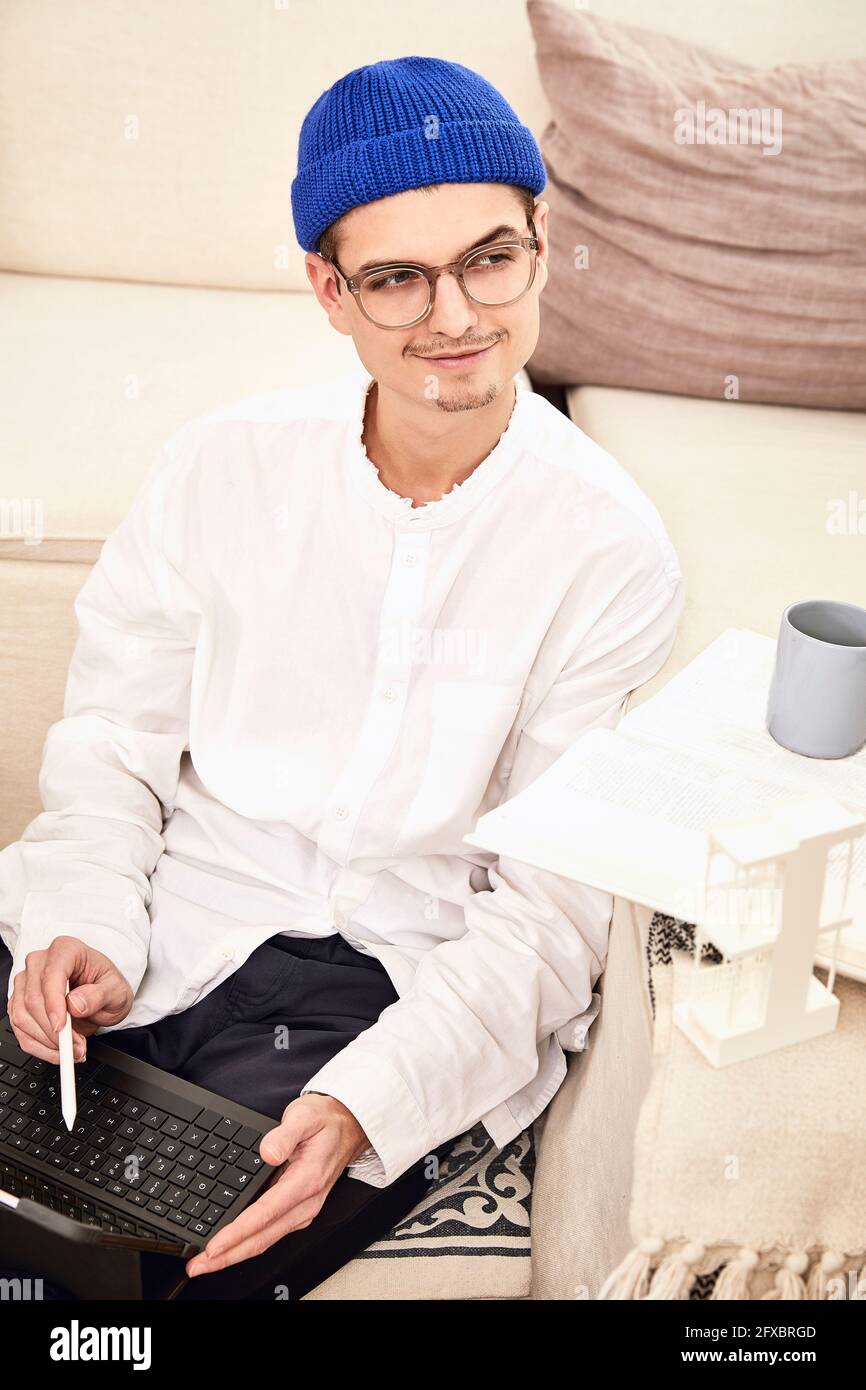 Smiling man looking away while sitting with digital tablet at home Stock Photo