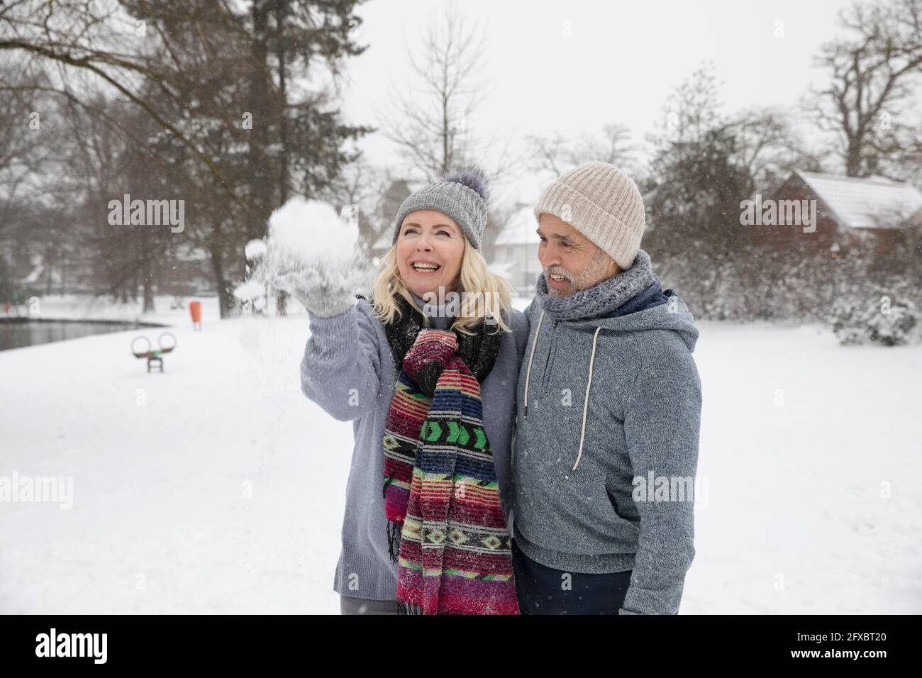Cheerful woman throwing snow while standing with man at park Stock Photo