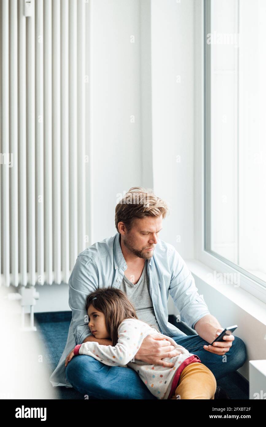 Man using mobile phone while daughter lying on lap at home Stock Photo