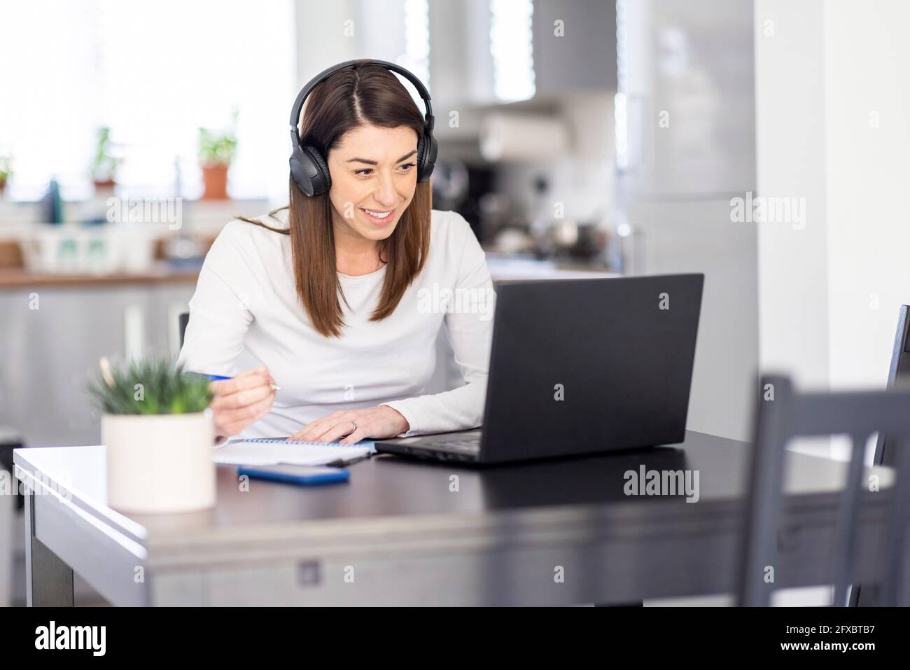 Smiling businesswoman writing note on diary during video conference while working at home Stock Photo