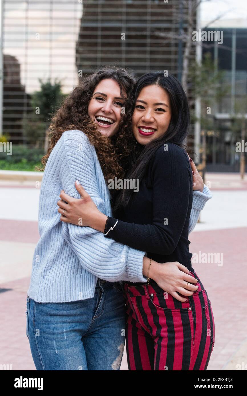 Smiling female friends hugging each other while standing outdoors Stock Photo