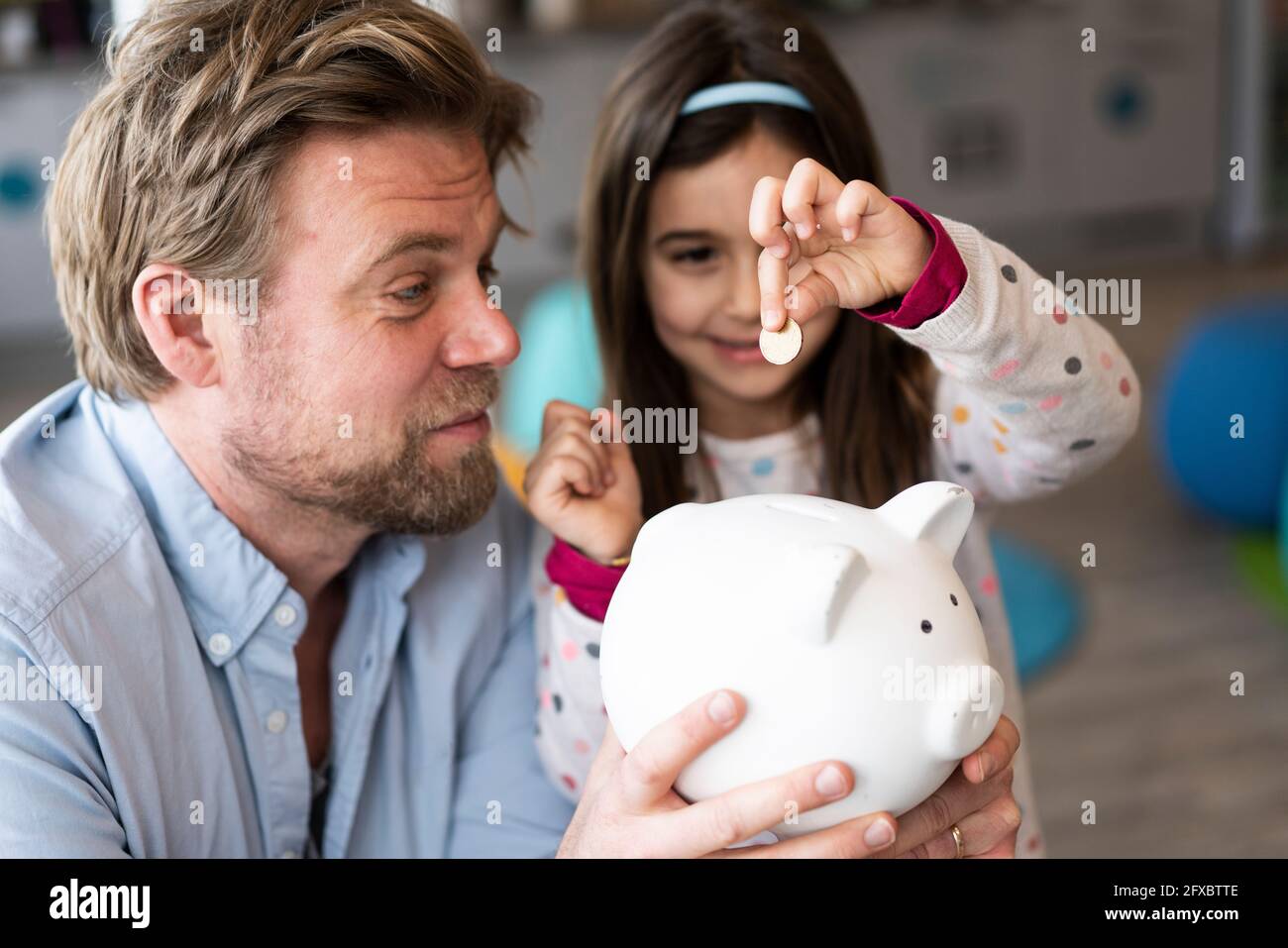 Daughter putting coin in piggy bank held by father at home Stock Photo ...