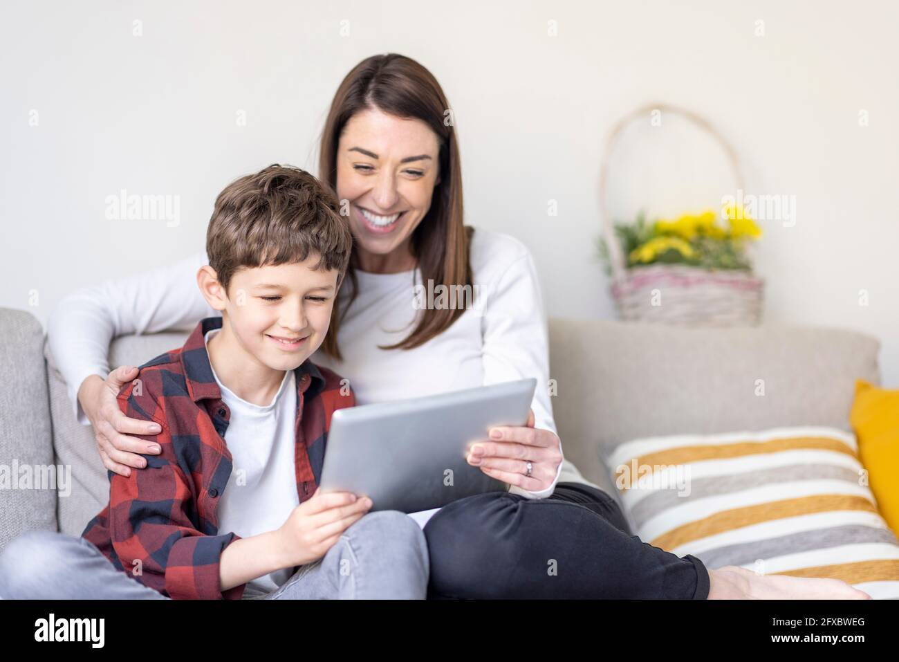Smiling boy and mother using digital tablet on sofa at home Stock Photo