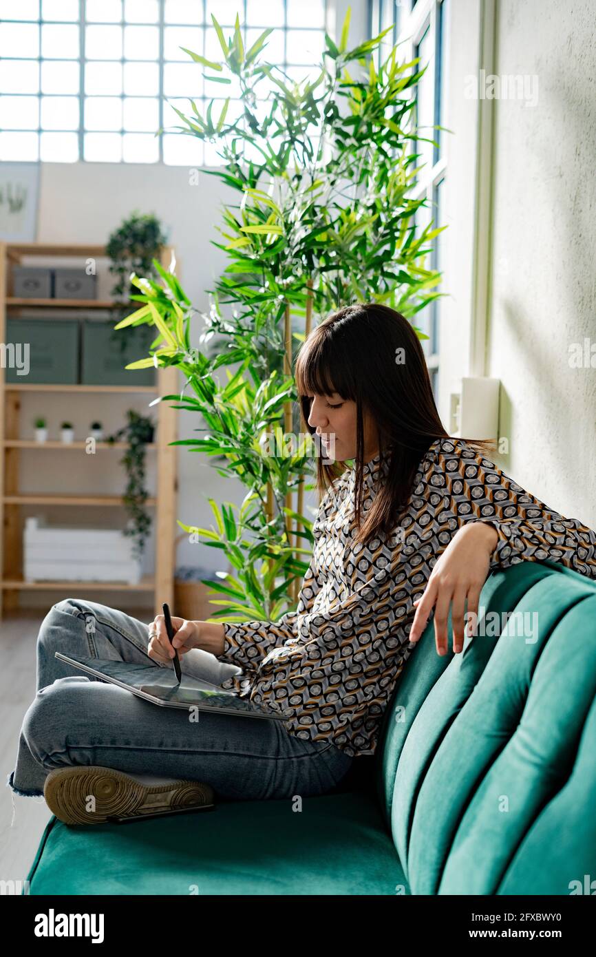 Female graphic designer using tablet while sitting on sofa at office Stock Photo
