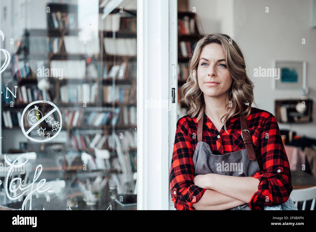 Thoughtful female waitress with arms crossed standing at cafe entrance ...