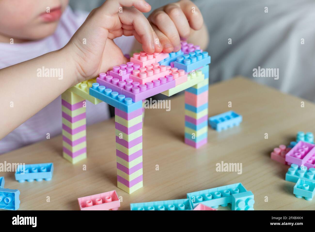 Little beautiful child playing with toy plastic building blocks, sitting at the table. Small girl busy with fun creative leisure activity. Development Stock Photo