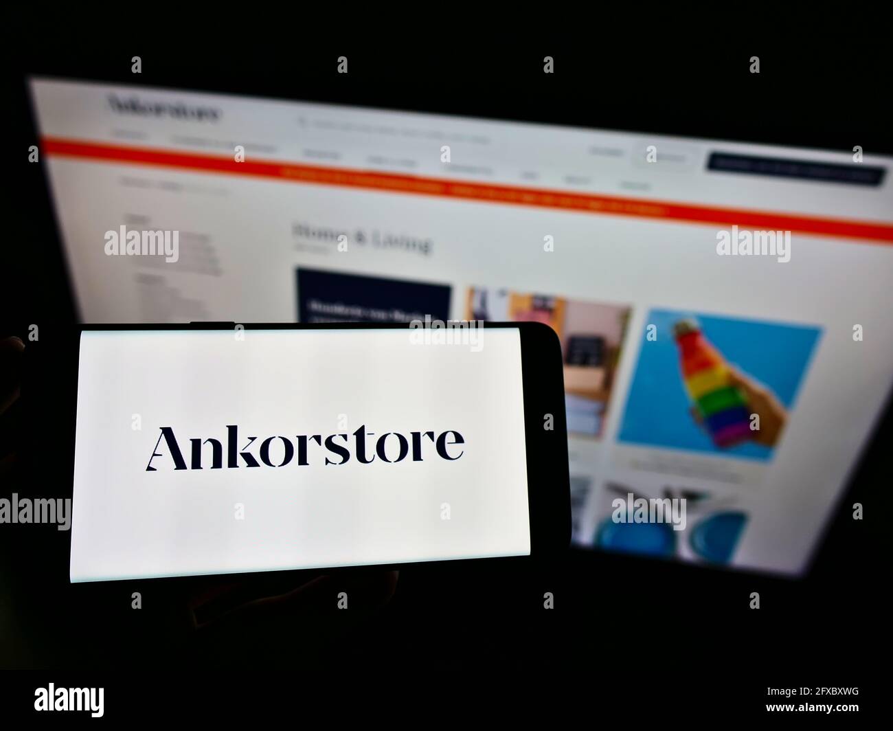 Person holding cellphone with logo of French online B2B wholesale company Ankorstore SAS on screen in front of web page. Focus on phone display. Stock Photo
