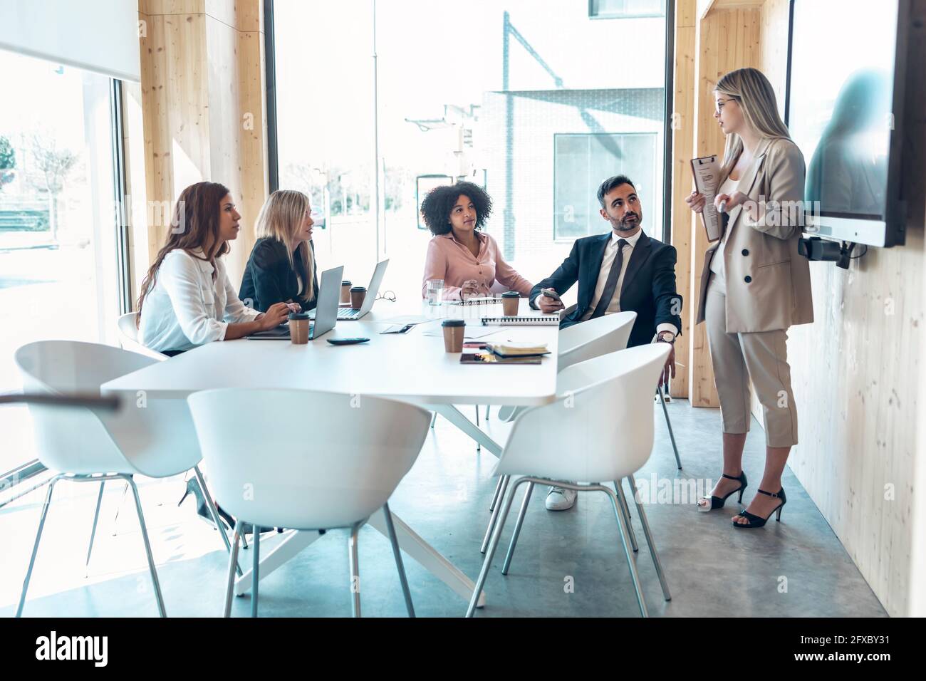 Female entrepreneur explaining to multi-ethnic coworkers in office Stock Photo