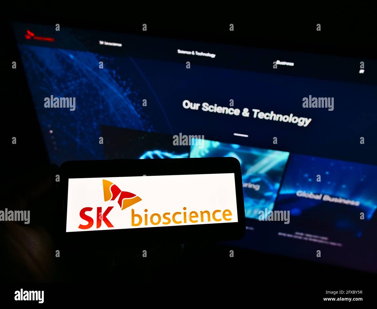 Person holding mobile phone with logo of South Korean biological company SK Bioscience Co Ltd on screen in front of webpage. Focus on phone display. Stock Photo